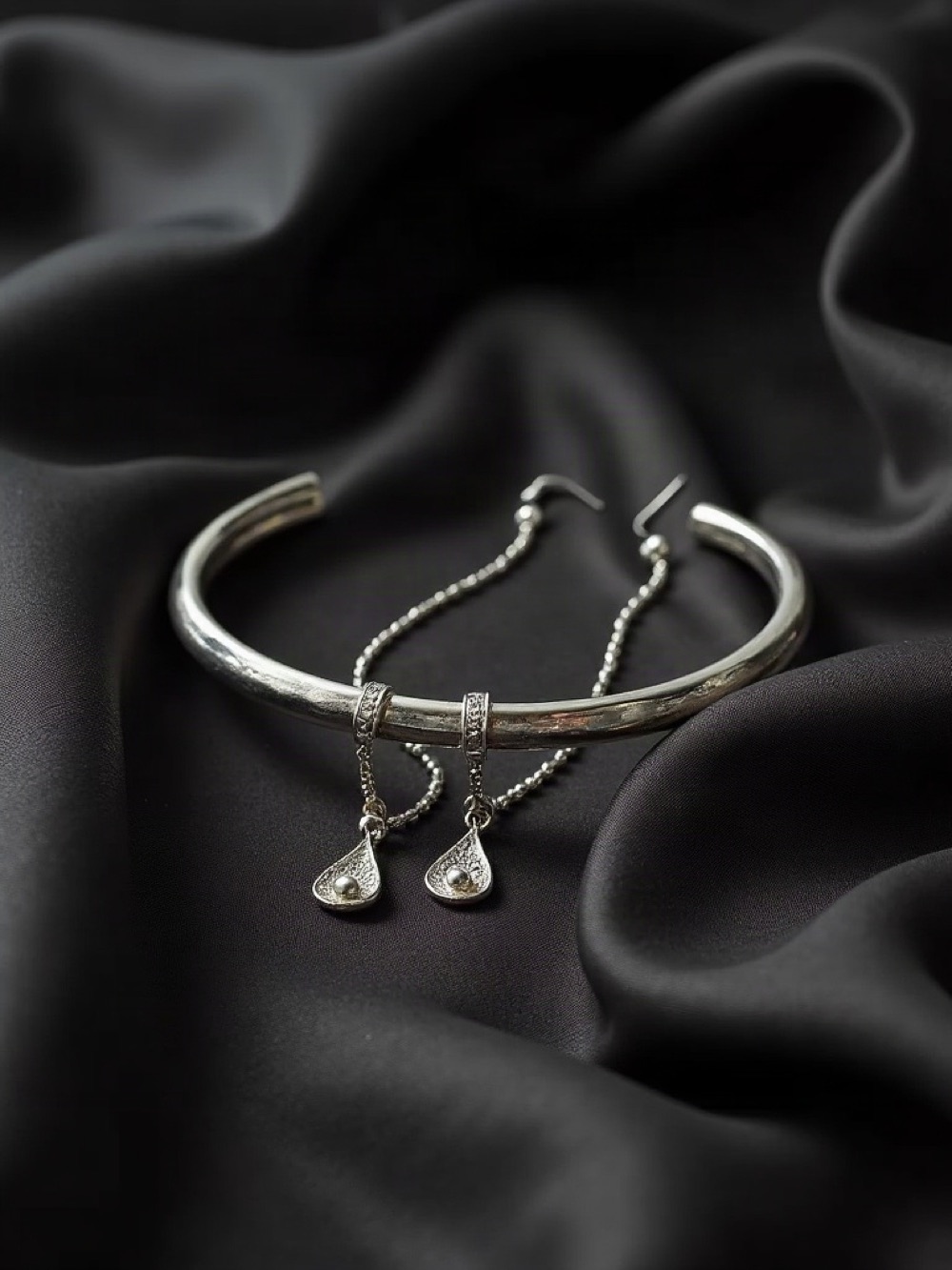 Silver cuff, earrings, and a fine chain on charcoal linen